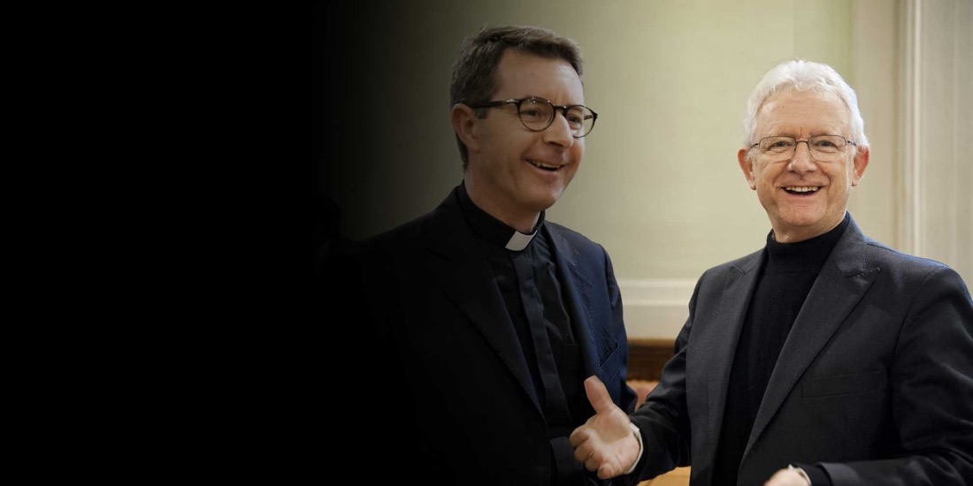Deux prêtres se saluent en souriant.